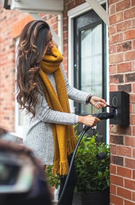 Women with yellow scarf charging blue electric vehicle.